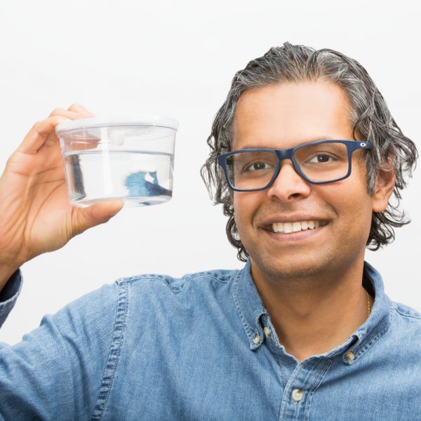 Man holding cup containing blue beta fish in water